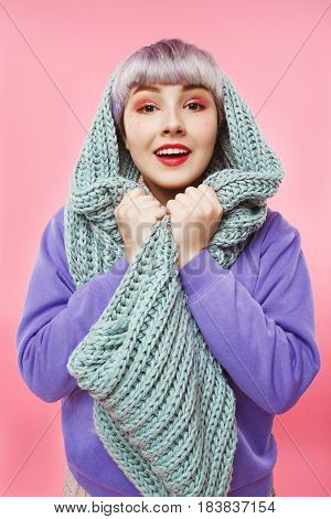 Close-up portrait of beautiful dollish girl with short light violet hair wearing lilac sweater and grey knitted neckwarmer over pink background. Copy space.