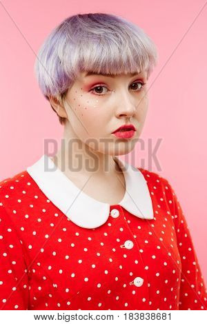 Close up portrait of beautiful dollish girl with short light violet hair wearing red dress over pink background. Copy space.