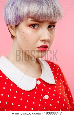 Close up portrait of beautiful dollish girl with short light violet hair wearing red dress over pink background. Copy space.
