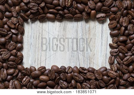 Roasted coffee beans around square space of wood, top view