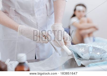 Dealing with injuries. Close up of a bandage lying on the table and being cut into pieces while being prepared for usage