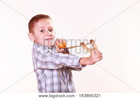 Nature and free time prankster little boy. Child have fun with wooden sling shot and fruit aim mandarine.