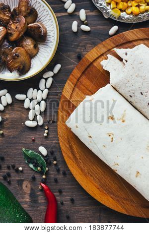 Vegetarian Burrito On Wooden Board Over Black Table Surrounded By Ingredients.