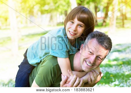 Portrait of father with his son having fun in summer park. Piggyback. Family fun. Happy boy playing with dad summer nature outdoor