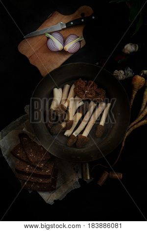 Still llife with raw morels, onion and rye bread on the dark background