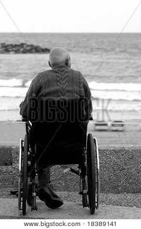 Old disabled man sitting on wheelchair and looking at the sea.