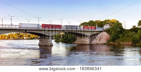 Heavy trucks with trailers are in queue on bridge on Russian-Estonian state transport-walking border. Reinforced concrete pontoon bridge over Narva river. Russia Ivangorod