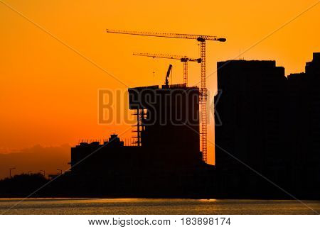 Silhouette of building under construction and the construction crane or power crane sunset time.