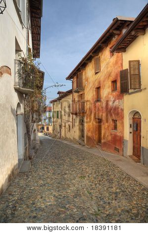 Vertikale orientiertes Bild der schmalen gepflasterten Straße zwischen alten bunten Häusern in Stadt Saluzzo, noch