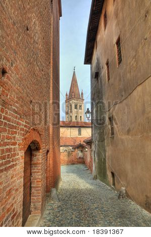 Vertikal orientierte Bild der schmalen gepflasterten Straße zwischen alten historischen Häusern in Saluzzo, Norditalien.