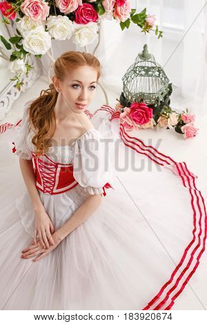 Cute ballerina in stage costumes and bouquets of spring flowers. Retro dress. She sits on the floor.