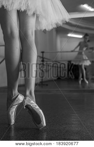 Ballerina in pointe shoes and tutu standing on toes at the bench. Reflection in the mirror in the ballet class. Classical ballet. Prima ballerina. Shooting close-up. Black and white photography
