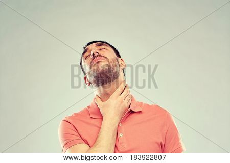 people, healthcare and problem concept - unhappy man touching his neck and suffering from throat pain over gray background