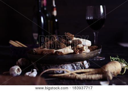 Still llife with raw morels in the copper bowl, onion and parsnip root on the dark background