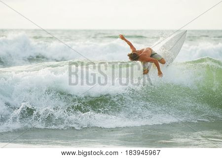 Surfer with a tanned body performs a trick on a short board - a jump over the waves. Extreme water sports, fun at the oceanfront surfing. The surfer rolls on the waves at sunset.