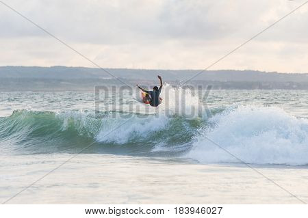 Surfer with a tanned body performs a trick on a short board - a jump over the waves. Extreme water sports, fun at the oceanfront surfing. The surfer rolls on the waves at sunset.