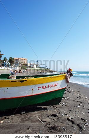 TORROX COSTA, SPAIN - OCTOBER 27, 2008 - Traditional wooden fishing boat on the beach with tourists to the rear Torrox Costa Malaga Province Andalusia Spain Western Europe, October 27, 2008.