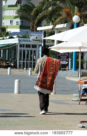 TORROX COSTA, SPAIN - OCTOBER 27, 2008 -Street seller walking along the promenade with rugs over his shoulder Torrox Costa Malaga Province Andalusia Spain Western Europe, October 27, 2008.