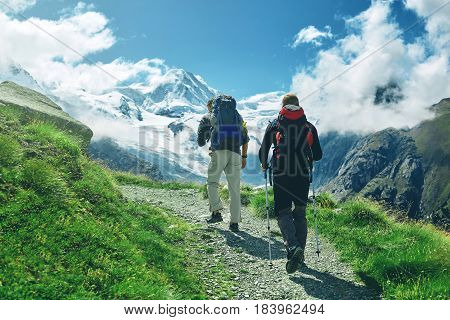 hikers with backpacks on the trail in the Apls, Swiss mountains. Trek near Matterhorn mount, mountain ridge on background