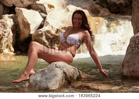Young busty woman sitting in underwear on a stone in the mountain stream while cooling.