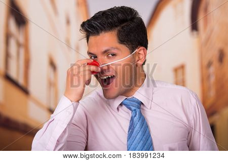 Funny handsome businessman touching his red plastic nose.