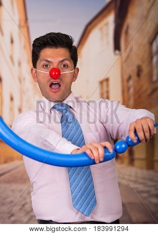 Funny handsome businessman with red plastic nose playing with a blue ballon
