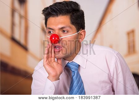 Funny handsome businessman with red plastic nose whispering a gossip.