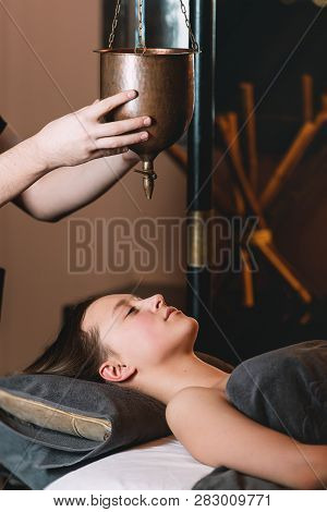 Specialist Making Shirodhara Massage Form Of Ayurveda Therapy. Beautiful Woman Spending Time At Mode