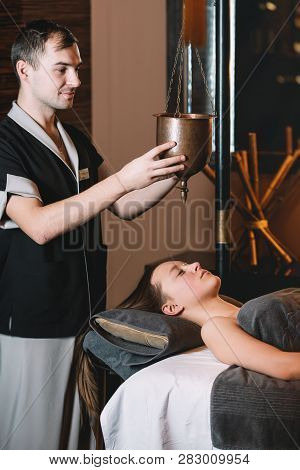Specialist Making Shirodhara Massage Form Of Ayurveda Therapy. Beautiful Woman Spending Time At Mode