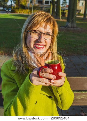 Young Blonde Girl In Cout With A Eyeglasses Standing Outdoor With Mug Of Hot Drink In Her Hands