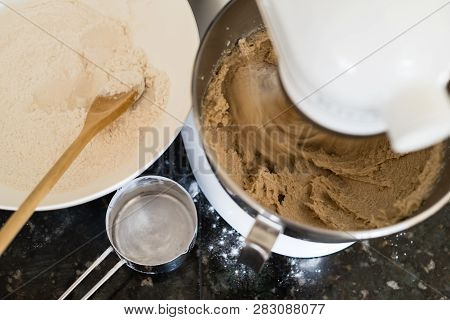 Overhead Shot Of Mixing Cookie Batter In A Stand Mixer With Flour In A Bowl And A Metal Measuring Cu