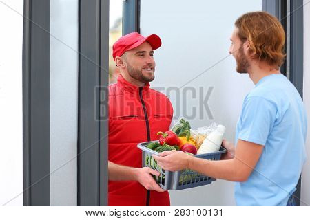 Courier Giving Plastic Crate With Products To Customer At Home. Food Delivery Service