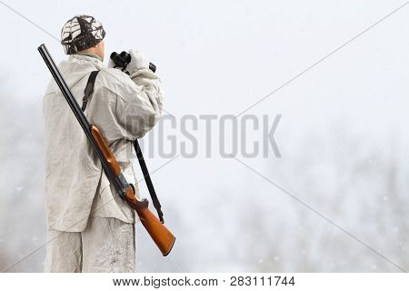 Hunter In White Camouflage With Binoculars In Winter Field