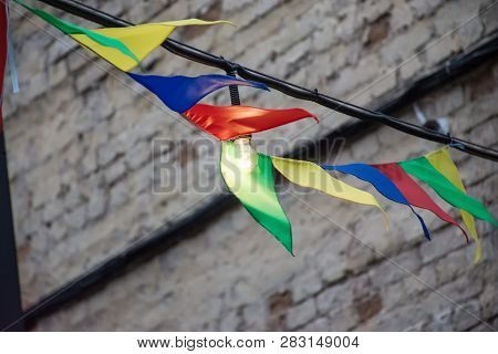 Glowing Light Bulb Surrounded By Colorful Flags That Flutter In The Wind. A Scene From A Holiday Or 