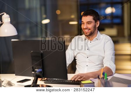 business, overwork, deadline and people concept - happy businessman with computer working at night office