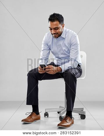 business, furniture and people concept - smiling indian businessman sitting on office chair over grey background