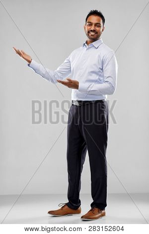 business, office worker and people concept - happy indian businessman showing something imaginary over grey background