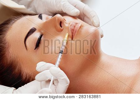 Portrait Of Beautiful Woman Gets Injection Of Botox In Her Lips. Closeup Hand In Glove With Syringe 