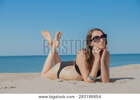 Beautiful Young Woman In Swimsuit At Sand Sea Beach Lying Under Sun Rays Tanning