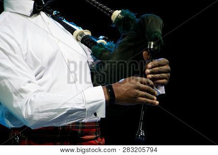 A Black Man In A White Shirt Plays The Scottish Bagpipe. Multicultural. On A Black Background.
