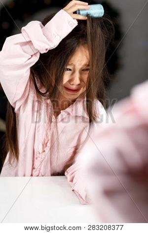 Crying Little Girl Tries To Remove The Hair Curlers Herself In Front Of The Mirror At Home