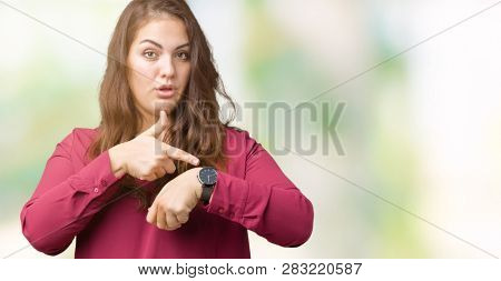 Beautiful plus size young woman over isolated background In hurry pointing to watch time, impatience, upset and angry for deadline delay