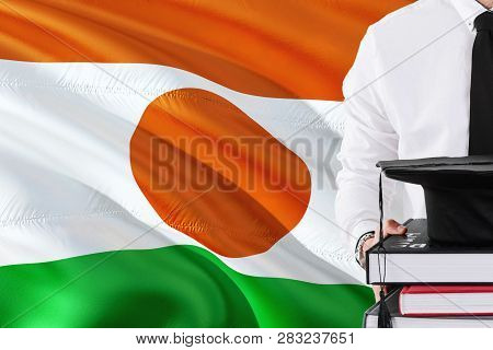 Successful Nigerien Student Education Concept. Holding Books And Graduation Cap Over Niger Flag Back