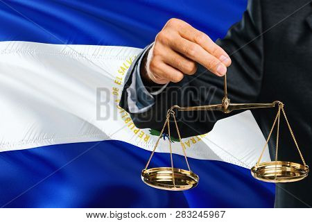 Salvadoran Judge Is Holding Golden Scales Of Justice With El Salvador Waving Flag Background. Equali