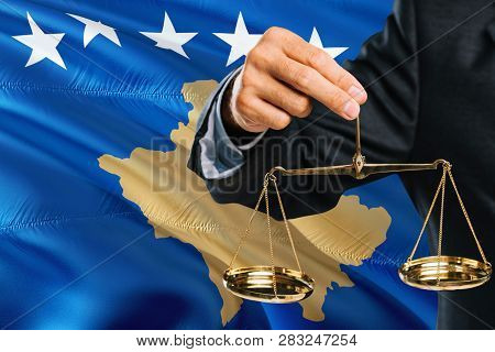 Judge Is Holding Golden Scales Of Justice With Kosovo Waving Flag Background. Equality Theme And Leg