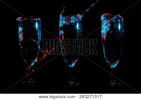 Row Of Three Identical Glasses With Clear Liquid Being Poured Into Them And Splashing Under Blue And