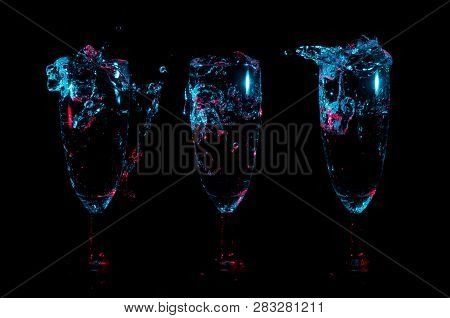 Blue Lights With Red Accents Highlight Splashes And Bubbles Of Liquid Into A Row Of Three Identical 