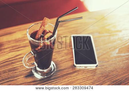 Close Up Of Glass Of Hot Mulled Wine And Smartphone With Black Screen On Wooden Table Top. Enjoying 