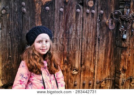 Portrait of cute little girl in black hat. She's got your old wooden door.