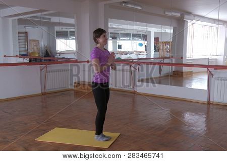 A Woman In A Pink T-shirt Is Standing In A Traditional Yoga Pose In A Gymnasium With Mirrors. Sports